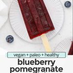 Overhead view of healthy blueberry pomegranate popsicles on coasters with fresh blueberries scattered around with text overlay that reads "paleo + vegan + healthy blueberry pomegranate popsicles: refreshing + simple + delicious!"