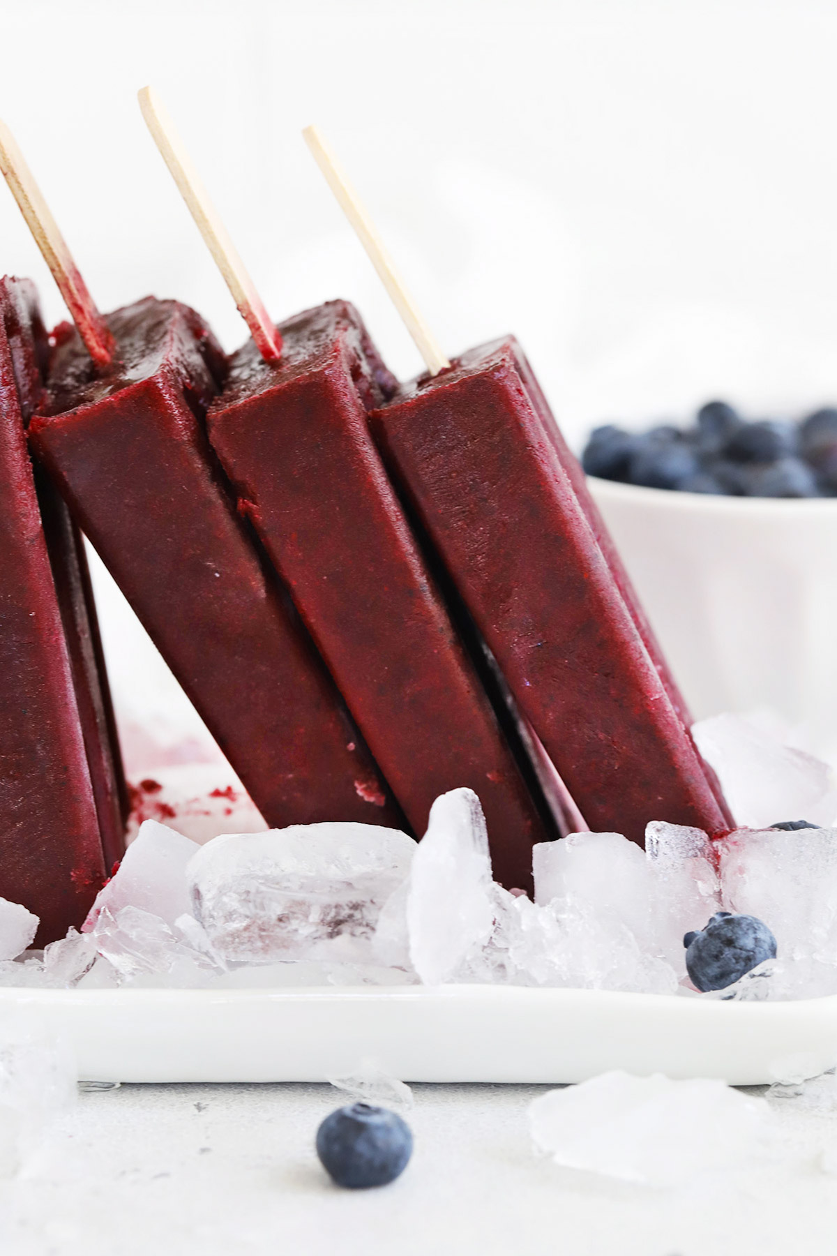 Front view of homemade blueberry pomegranate popsicles standing upright on a platter of ice