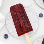 Overhead view of healthy blueberry pomegranate popsicles on coasters with fresh blueberries scattered around