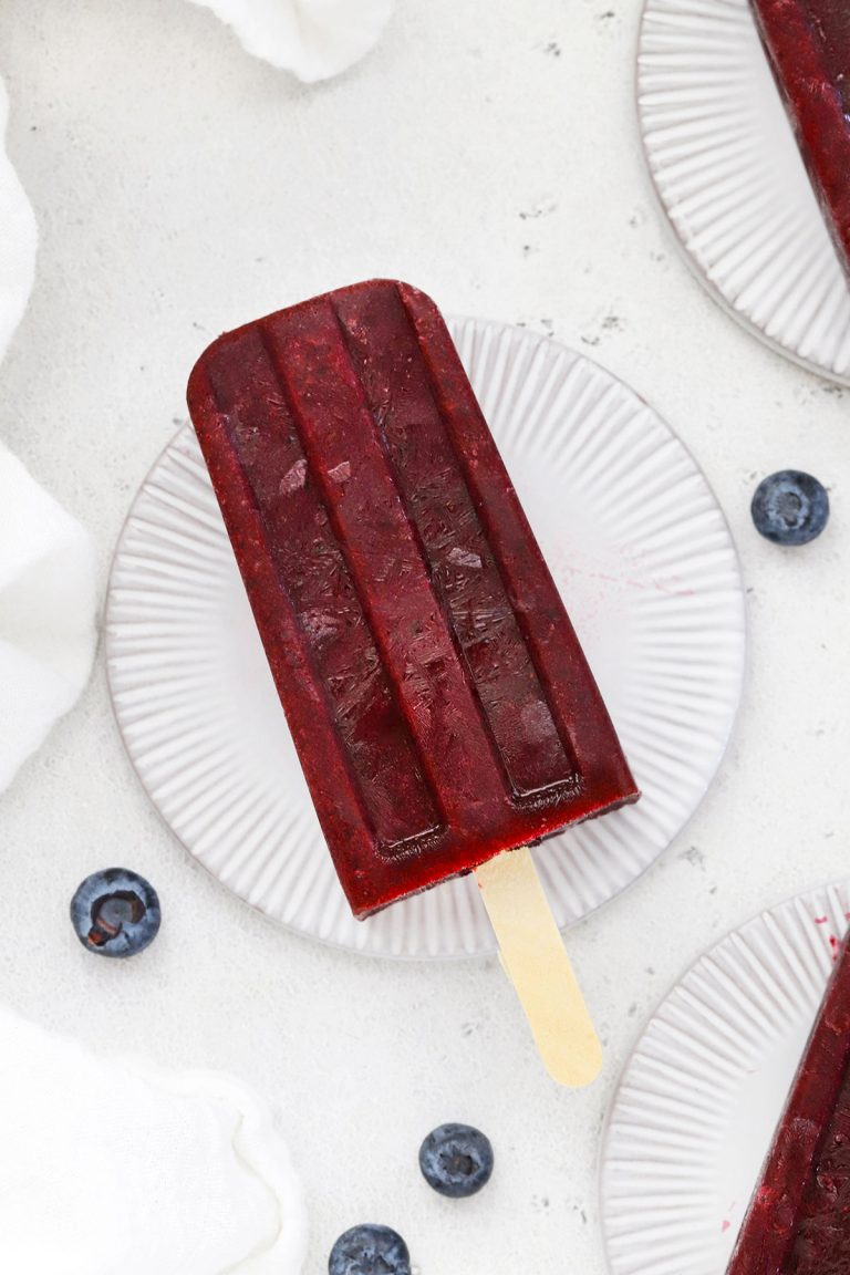Overhead view of healthy blueberry pomegranate popsicles on coasters with fresh blueberries scattered around