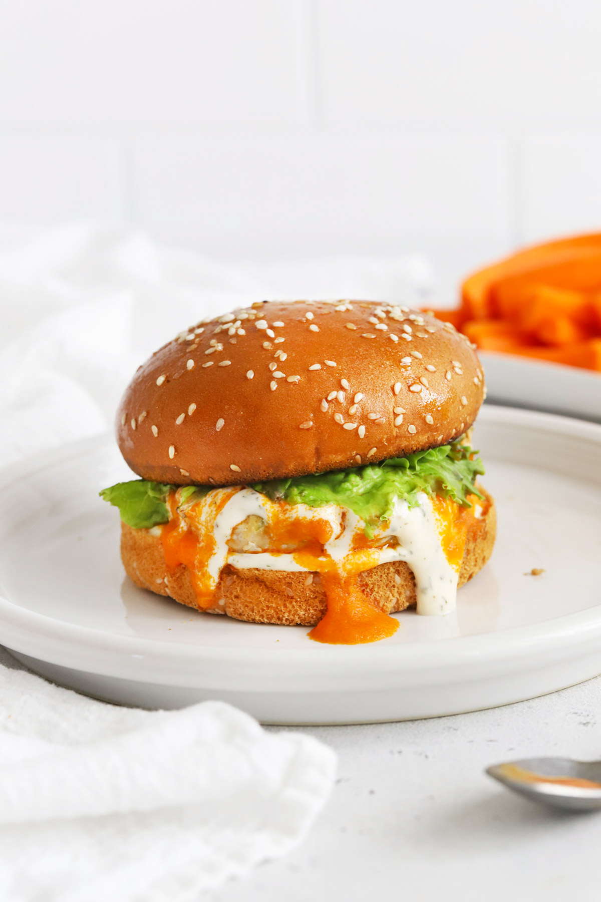 Front view of a buffalo chicken burger on a gluten-free bun with lettuce, buffalo sauce, and paleo ranch.