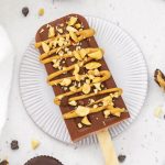 Overhead view of a chocolate peanut butter popsicle drizzled with natural peanut butter and sprinkled with crushed peanuts