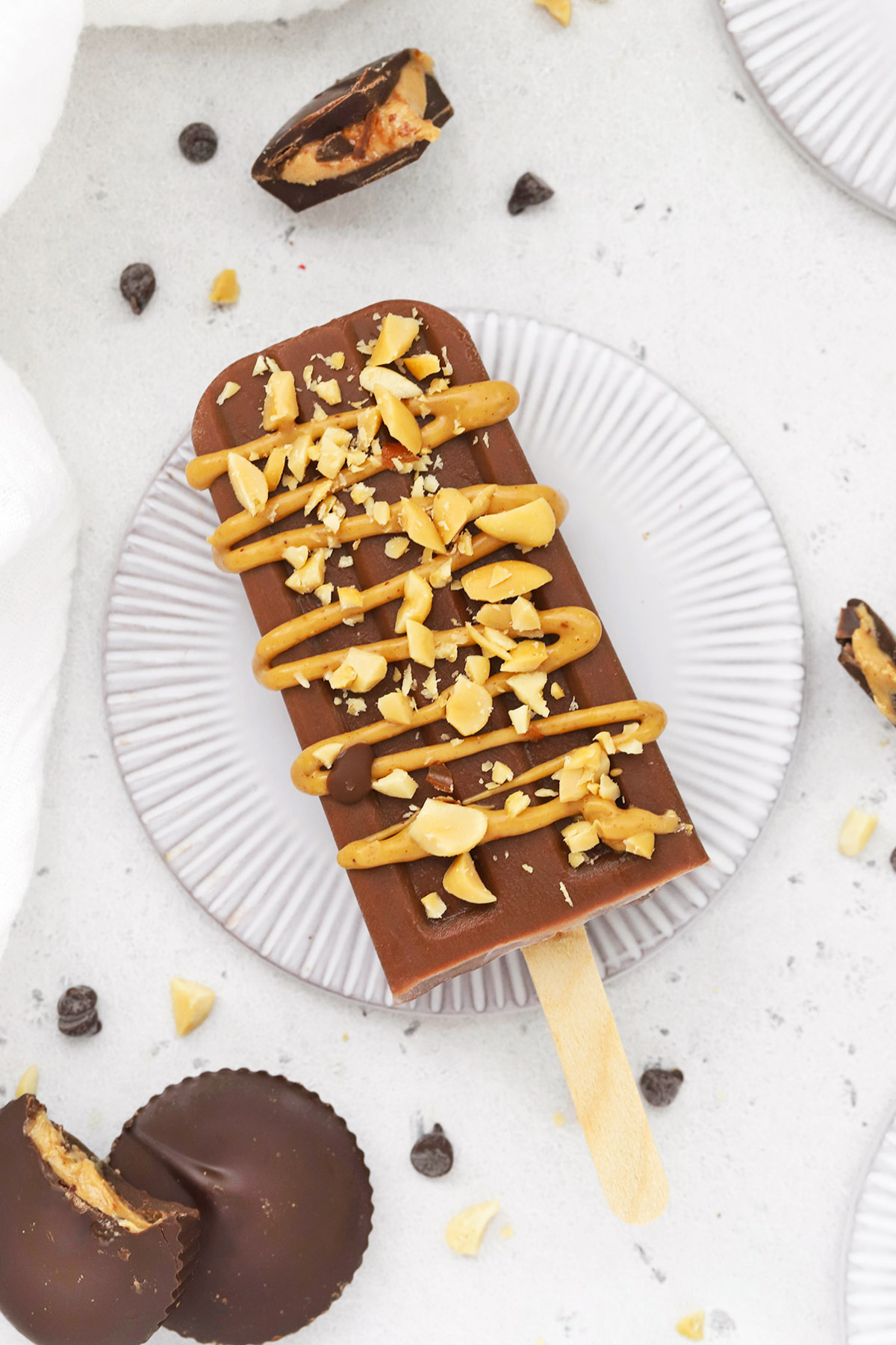 Overhead view of a chocolate peanut butter popsicle drizzled with natural peanut butter and sprinkled with crushed peanuts