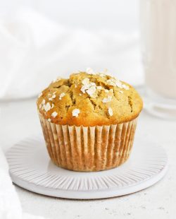 Front view of a banana oatmeal muffin on a coaster with a glass of almond milk in the background