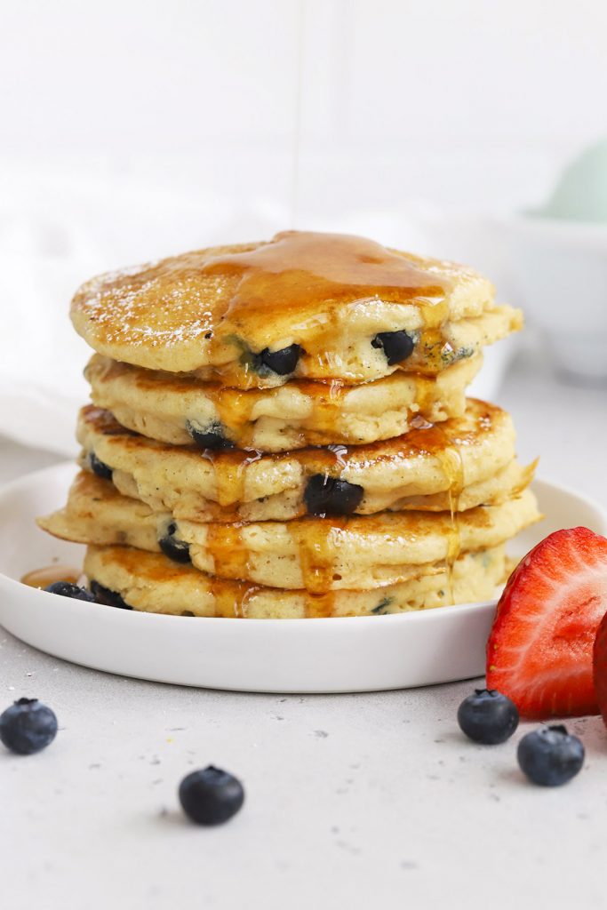 Front view of a stack of fluffy gluten-free blueberry pancakes being drizzled with syrup