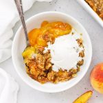 Overhead view of a bowl of gluten-free peach crisp topped with dairy-free vanilla ice cream, slowly melting over the warm crisp