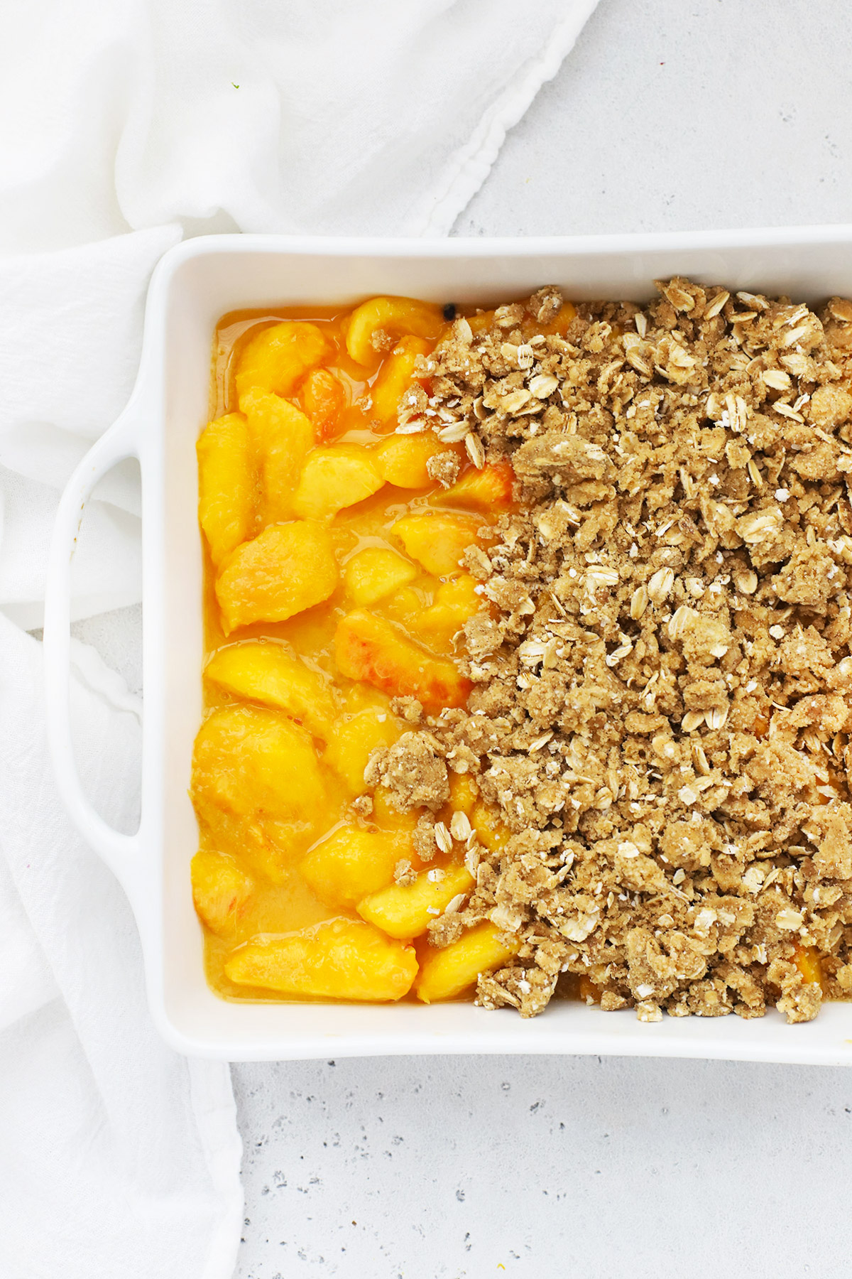 Overhead view of gluten-free peach crisp being topped with crumble topping