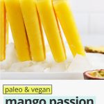 Front view of a row of mango passion fruit popsicles standing up on a plate of ice with text overlay that reads paleo & vegan mango passion fruit popsicles: 3-ingredients + delicious"