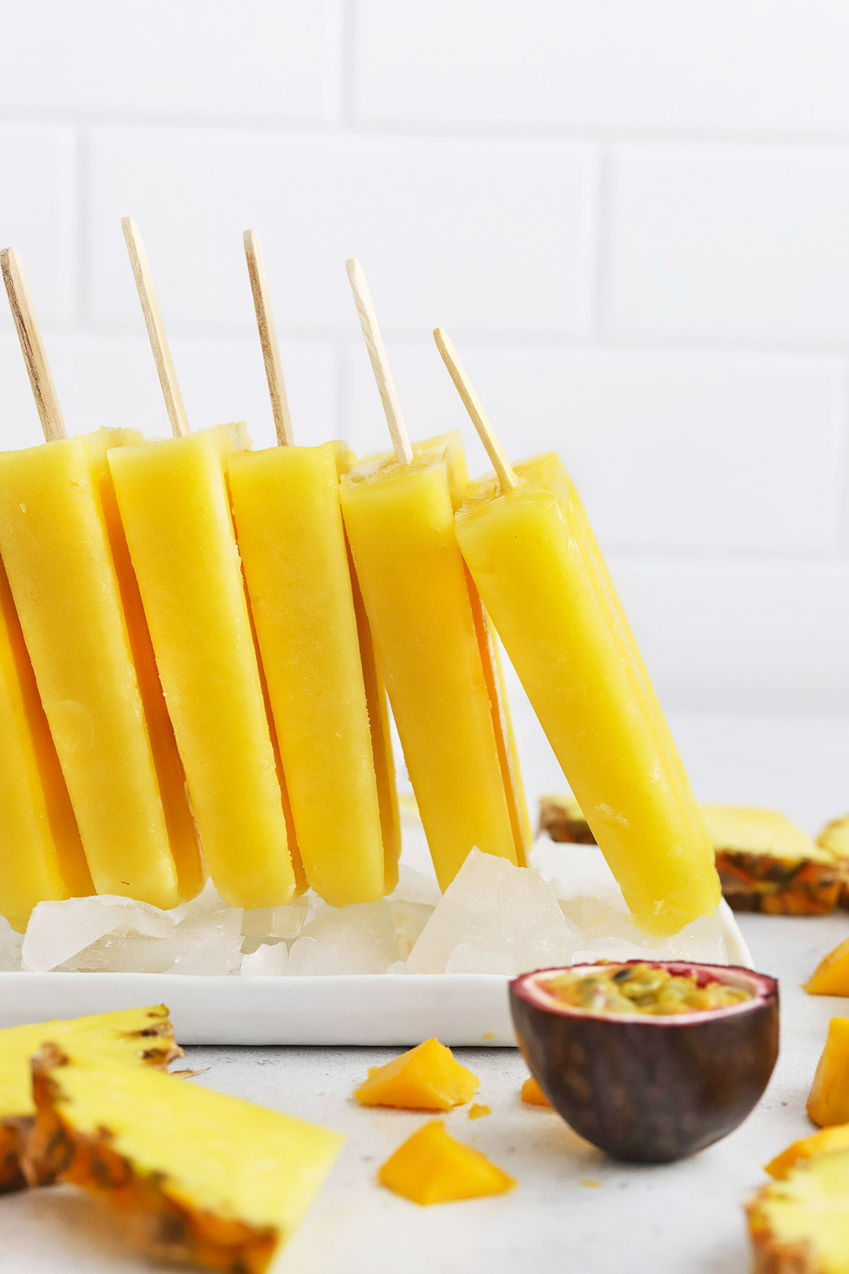 Front view of a row of mango passion fruit popsicles standing up on a plate of ice