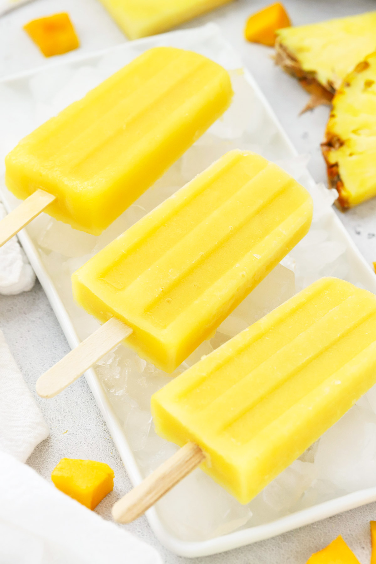 Front view of three mango passion fruit popsicles laying on a plate of ice