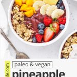 Overhead up view of a fresh pineapple acai bowl topped with fresh berries, bananas, pineapple, mango, and granola on a white background with text overlay that reads "vegan + paleo pineapple acai bowls: fresh + beautiful + healthy"