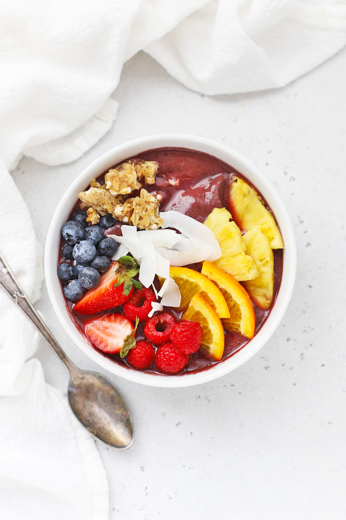 Overhead view of a pineapple acai bowl with fresh berries, pineapple, orange slices, shaved coconut, granola, mango on a white background
