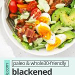 Overhead view of a blackened salmon cobb salad on a white background with avocado green goddess dressing on the side with text overlay that reads "paleo & whole30 blackened salmon cobb salad: A yummy healthy dinner"