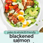 Overhead view of a blackened salmon cobb salad on a white background with avocado green goddess dressing on the side with text overlay that reads "paleo & whole30 blackened salmon cobb salad: A delicious healthy dinner"