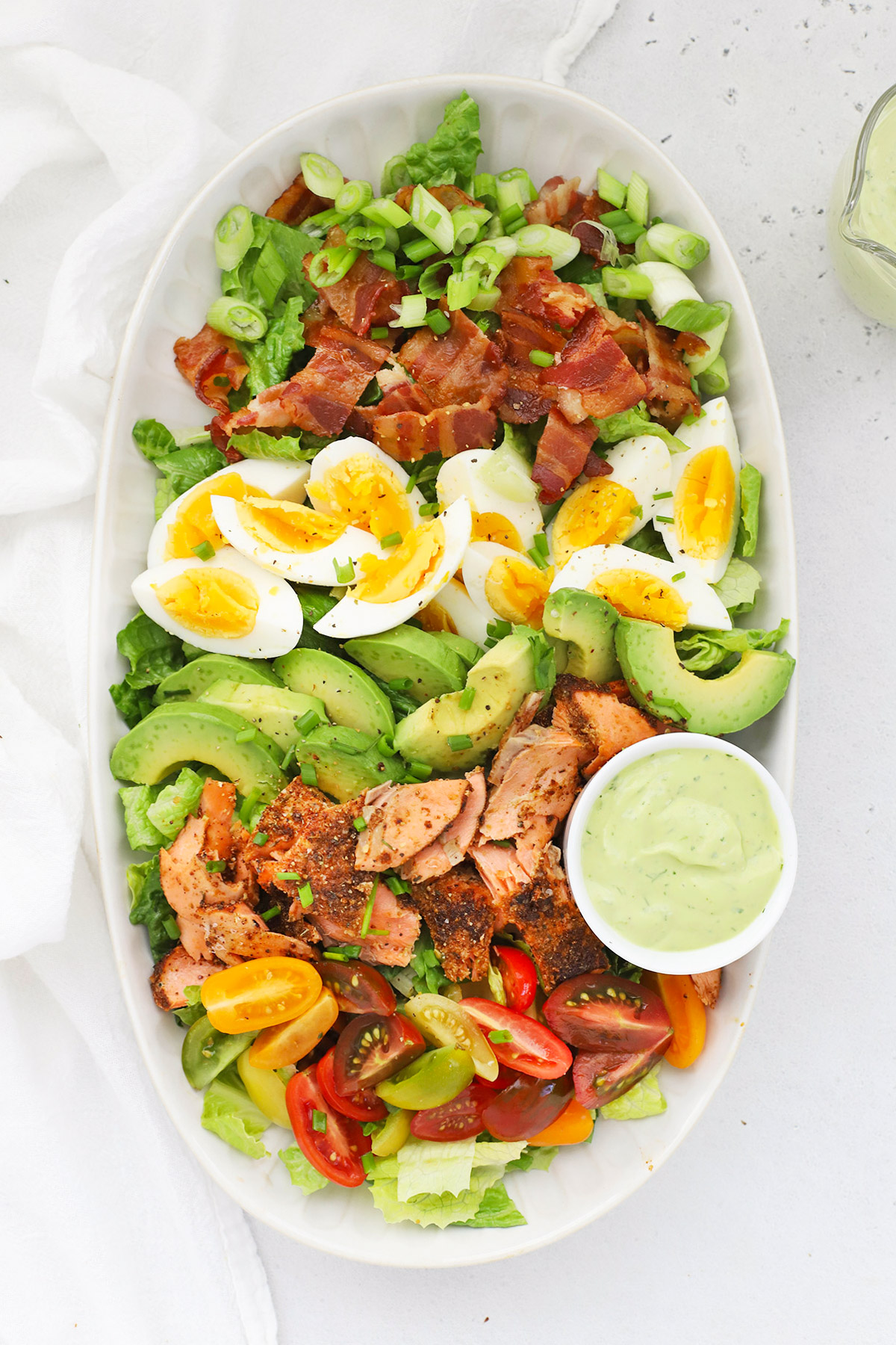 Overhead view of a big platter of blackened salmon cobb salad with colorful ingredients arranged in rows.