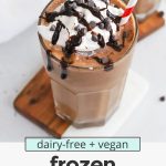 Front view of a glass of vegan frozen hot chocolate topped with coconut whipped cream and chocolate chips with text overlay that reads "dairy-free + vegan frozen hot chocolate: frosty + creamy + so delicious!"