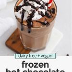 Front view of a glass of vegan frozen hot chocolate topped with coconut whipped cream and chocolate chips with text overlay that reads "dairy-free + vegan frozen hot chocolate: frosty + creamy + so delicious!"