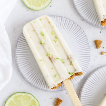 Overhead view of healthy key lime pie popsicles garnished with graham cracker crumbs and lime zest on a white background