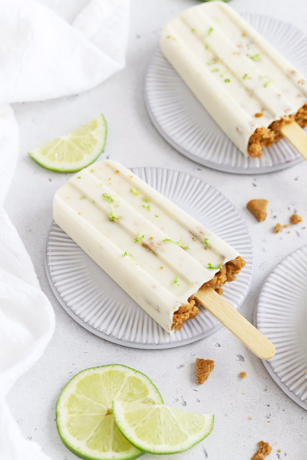 Front view of healthy key lime pie popsicles garnished with graham cracker crumbs and lime zest on a white background