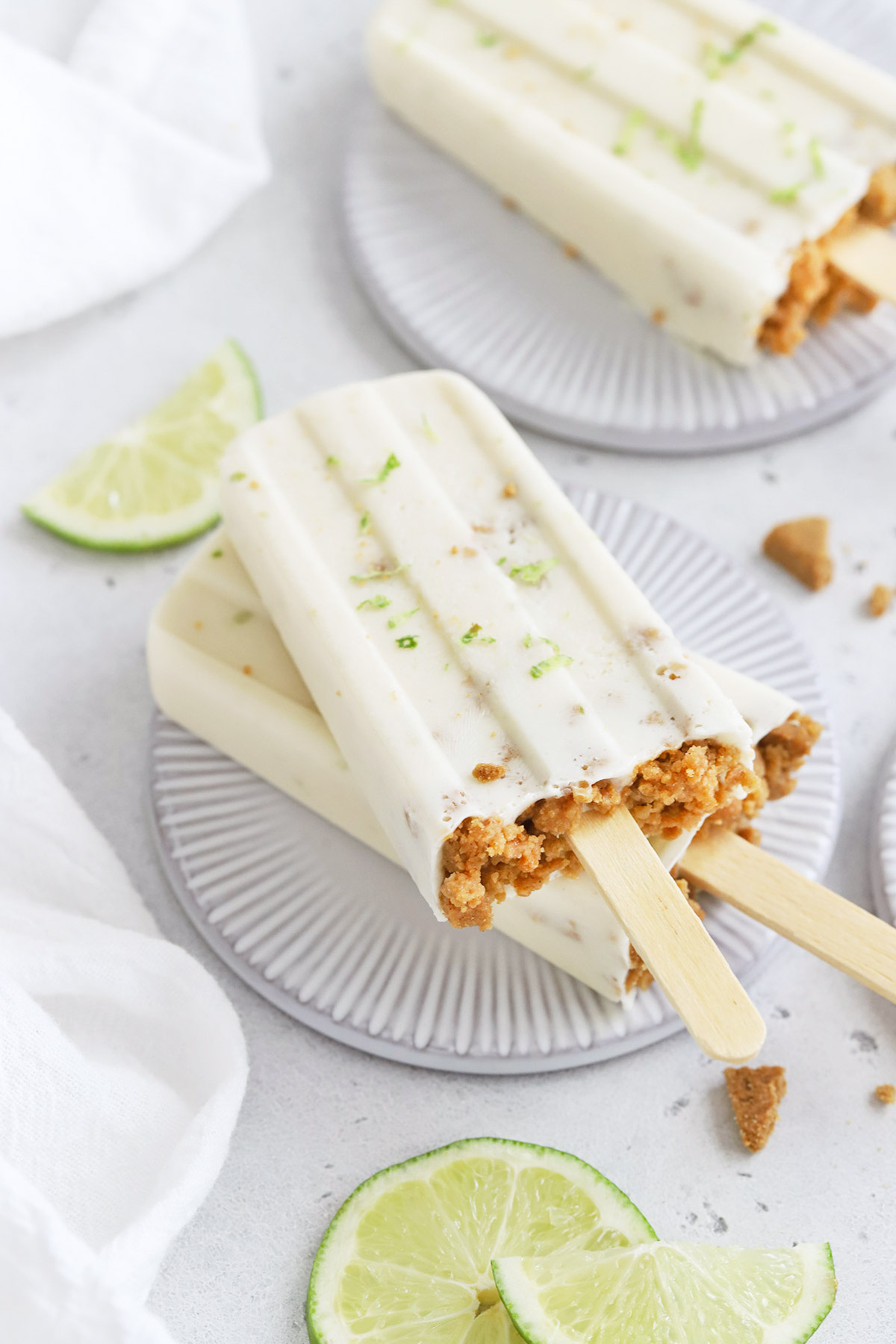Front view of healthy key lime pie popsicles garnished with graham cracker crumbs and lime zest on a white background