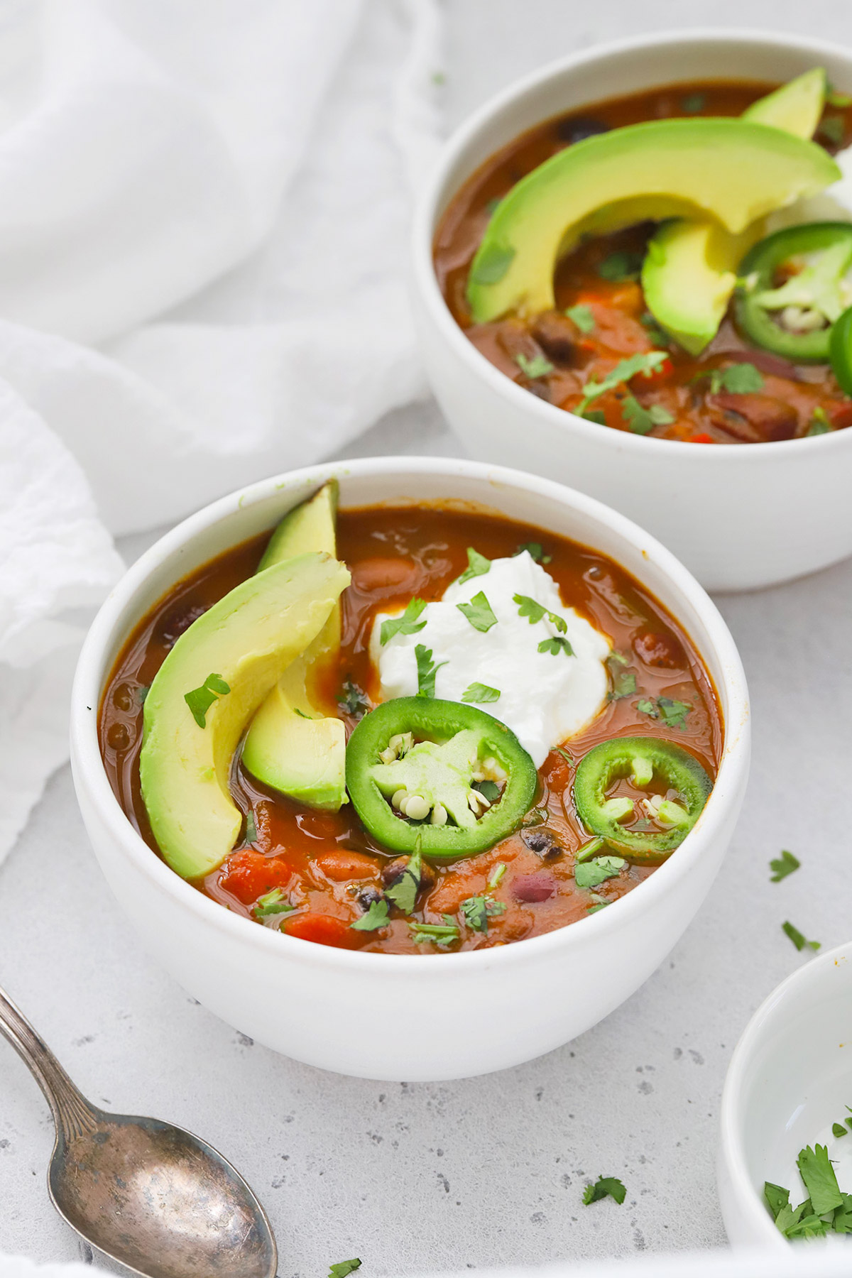 Front view of a bowl of vegetarian pumpkin chili topped with sour cream, jalapeño, and avocado