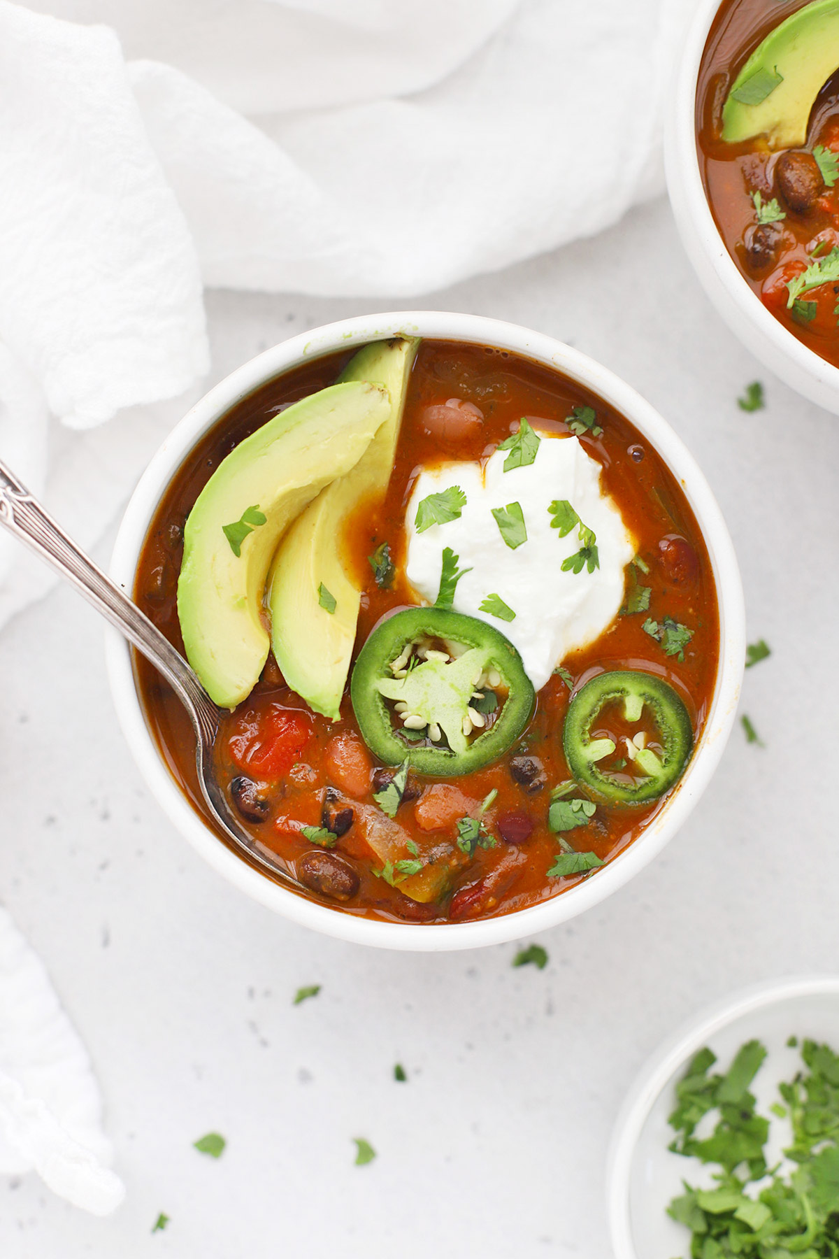 Overhead view of a bowl of vegetarian pumpkin chili topped with sour cream, jalapeño, and avocado