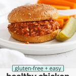 Front view of healthy chicken sloppy joes on gluten-free buns with a pickle wedge and carrot sticks with text overlay that reads "gluten-free + easy healthy chicken sloppy joes: a lighter take on the original"