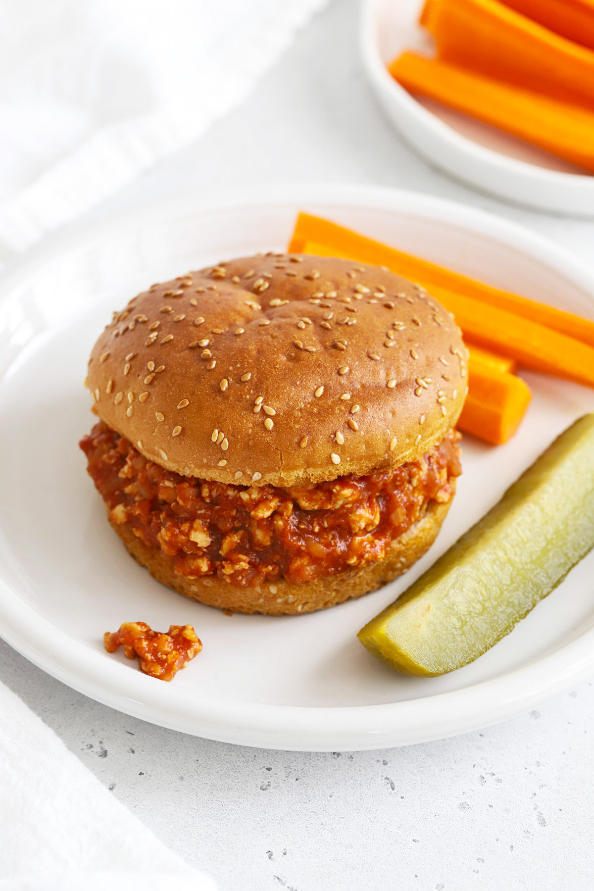 Front view of healthy chicken sloppy joes on gluten-free buns with a pickle wedge and carrot sticks