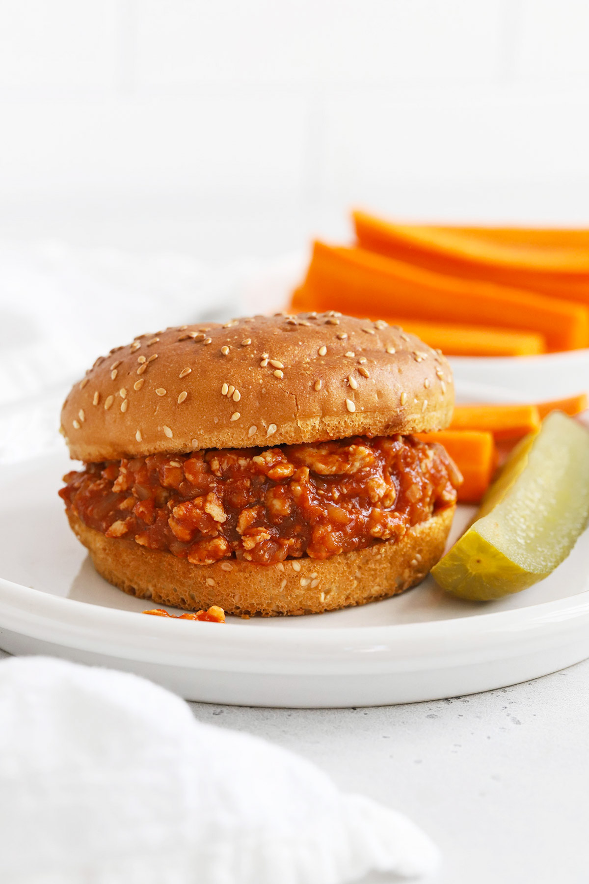 Front view of healthy chicken sloppy joes on gluten-free buns with a pickle wedge and carrot sticks