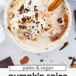 Overhead view of a steaming mug of dairy-free pumpkin spice hot chocolate topped with coconut whipped cream, shaved chocolate, and pumpkin spice with text overlay that reads "paleo & vegan pumpkin spice hot chocolate: cozy + creamy + amazing!"