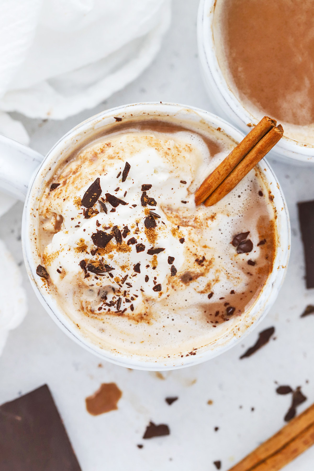 Overhead view of a steaming mug of dairy-free pumpkin spice hot chocolate topped with coconut whipped cream, shaved chocolate, and pumpkin spice