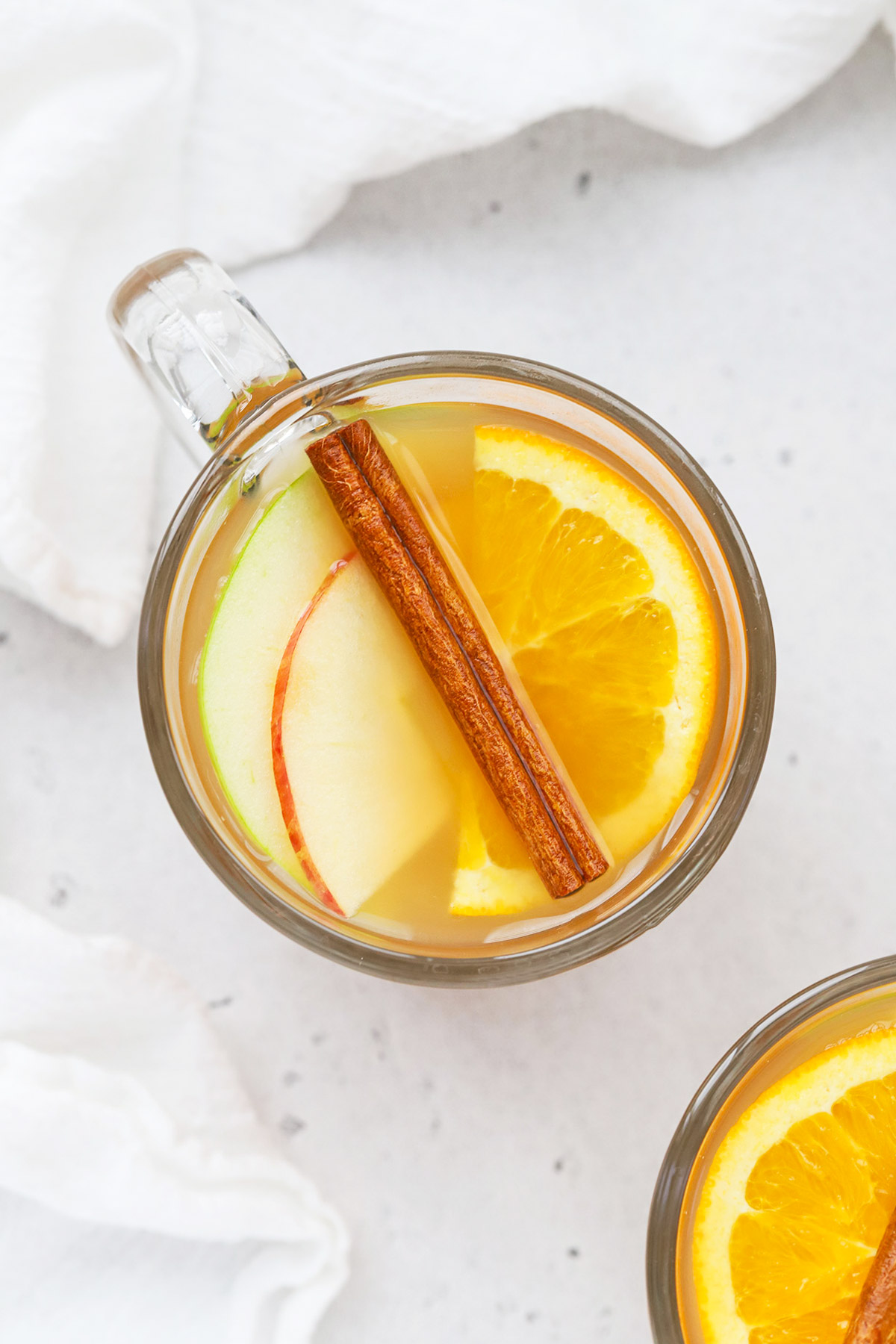 Overhead view of a glass mug of hot spiced cider garnished with apple slices, orange slices, and cinnamon sticks