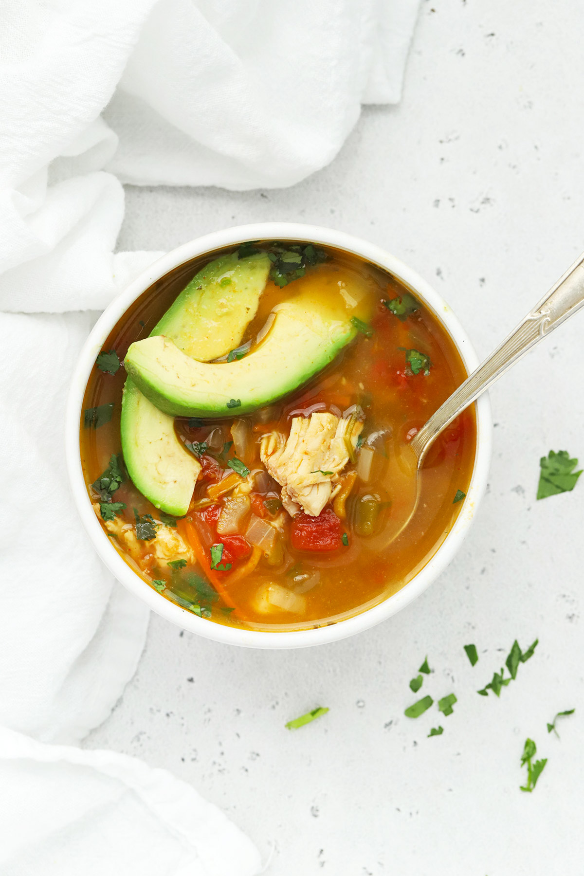 Overhead view of a bowl of chicken lime soup (sopa de lima) topped with avocado and cilantro