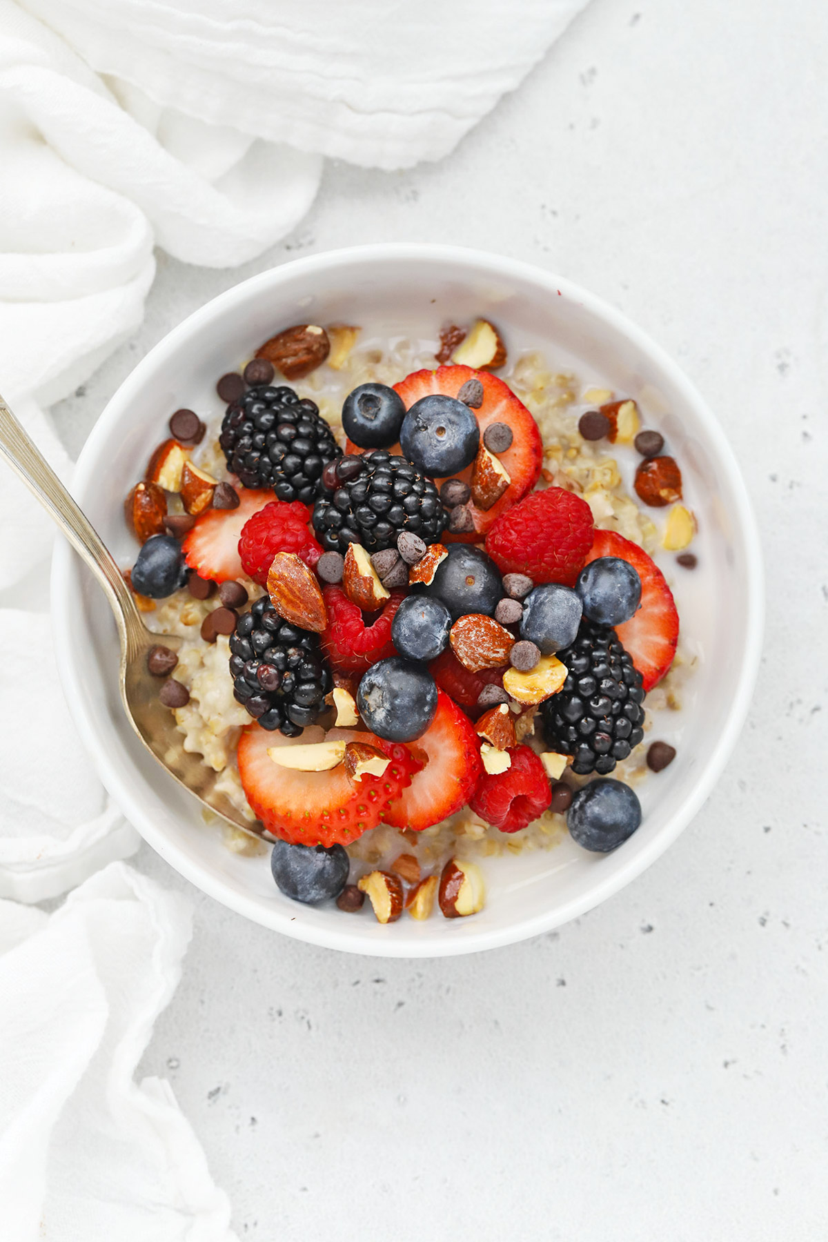 Overhead view of a bowl of stovetop steel-cut oats topped with fresh berries, almonds, and cacao nibs
