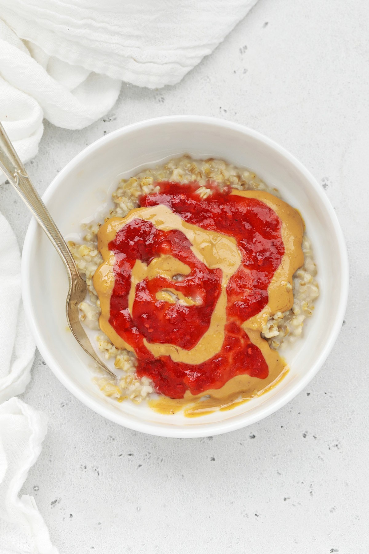 Overhead view of a bowl of stovetop steel-cut oats with peanut butter and raspberry jam