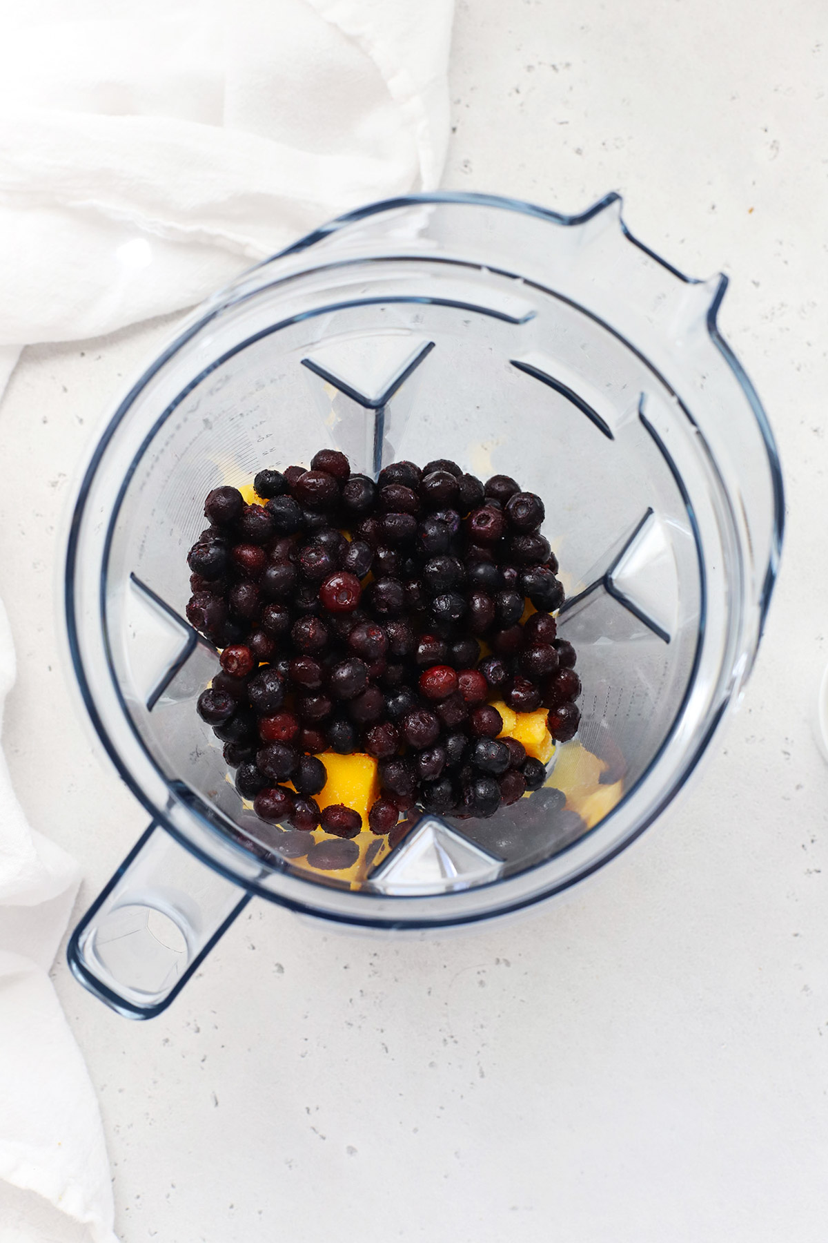 Adding fruit to the blender to make blueberry mango smoothie