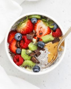 Overhead view of a white bowl of vanilla chia pudding topped with kiwi, fresh berries, peanut butter, and chocolate chunks