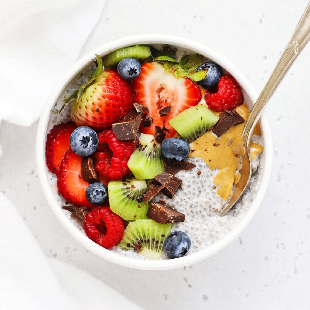 overhead view of a bowl of vanilla chia pudding topped with fresh berries, kiwi, cacao nibs, and peanut butter