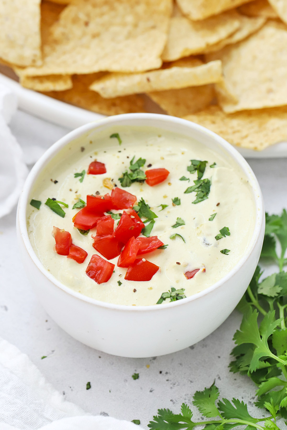 Front view of a white bowl of white cashew queso dip topped with chopped tomato and minced cilantro