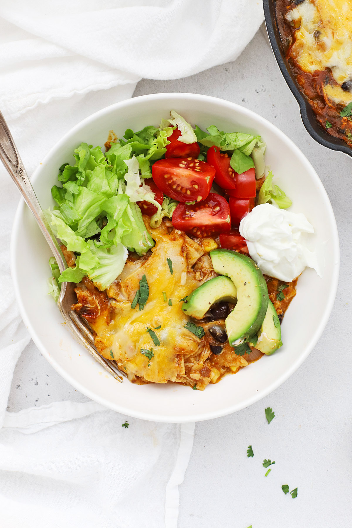 A bowl with a serving of chicken enchilada skillet, served with toppings like avocado, cilantro, lettuce, and tomato