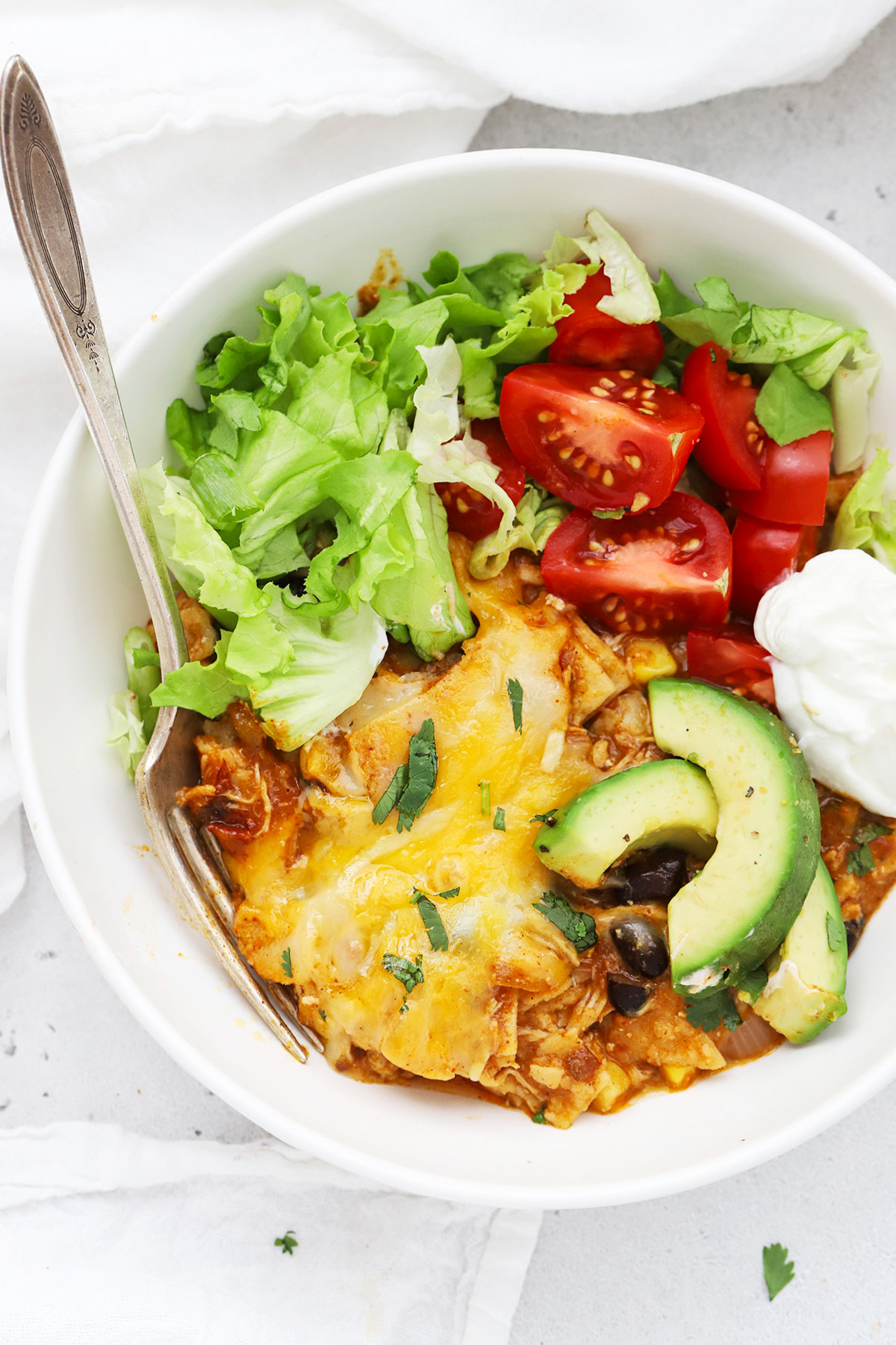 A bowl with a serving of chicken enchilada skillet, served with toppings like avocado, cilantro, lettuce, and tomato