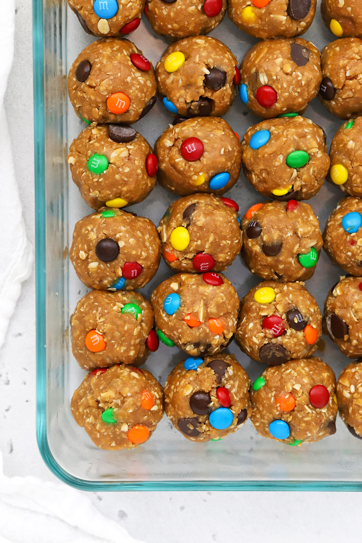 Overhead view of a glass container of peanut butter monster cookie energy bites with m&ms