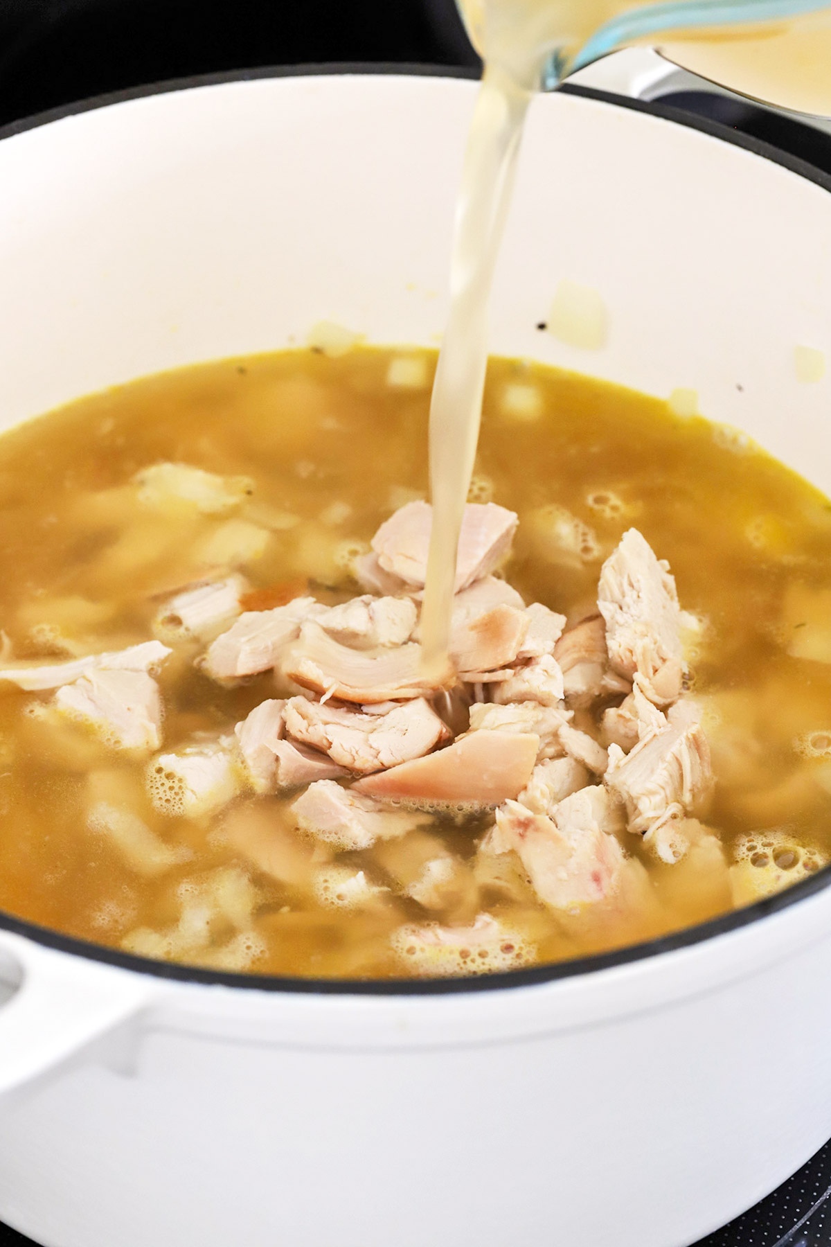 Pouring broth into a pot of gluten-free chicken soup