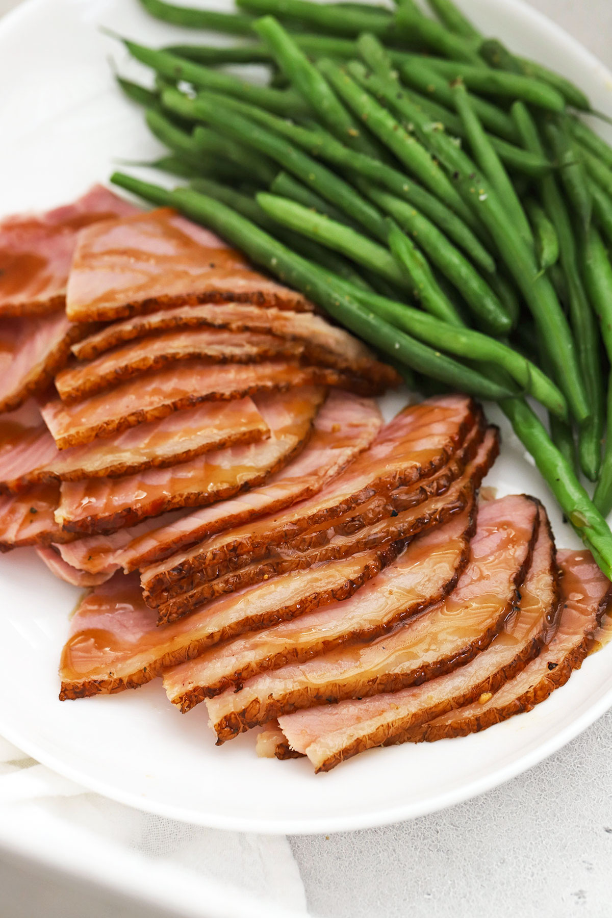 Slices of glazed ham on a white plate with steamed green beans