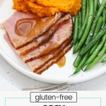 Slices of glazed ham on a white plate with mashed sweet potatoes and steamed green beans