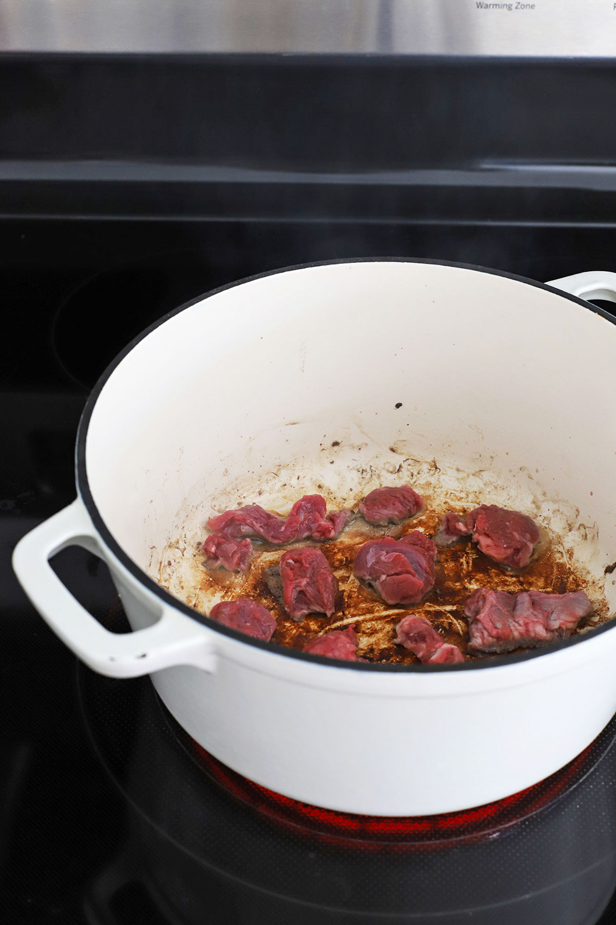 Browning stew beef cubes in a white Dutch oven