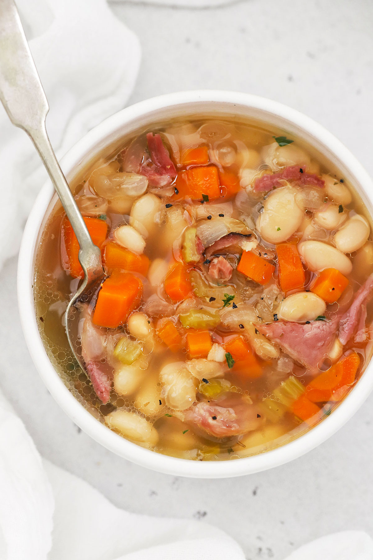 A spoon dipping into a white bowl of crock pot ham and bean soup