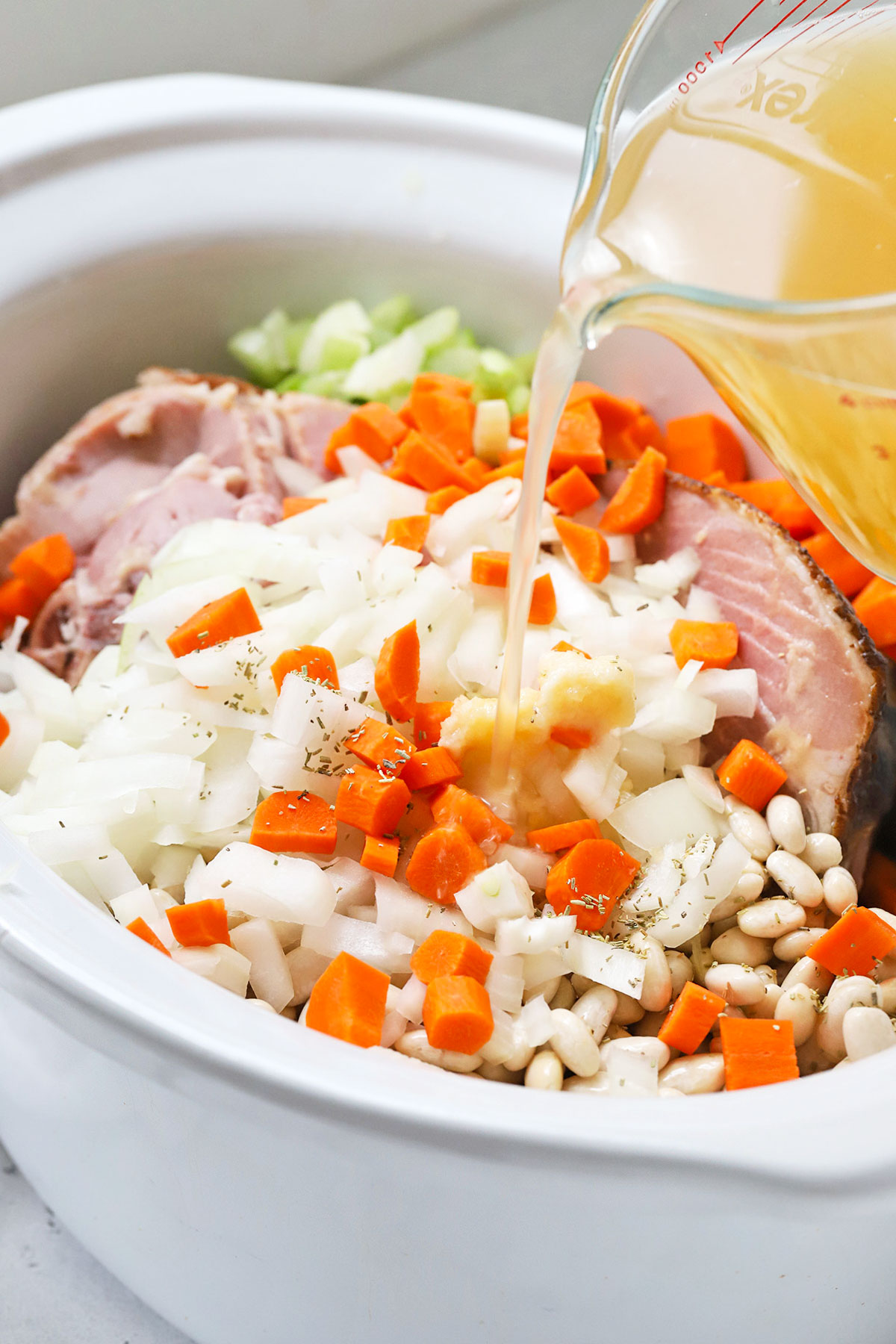 Pouring broth over veggies to make crock pot ham and bean soup