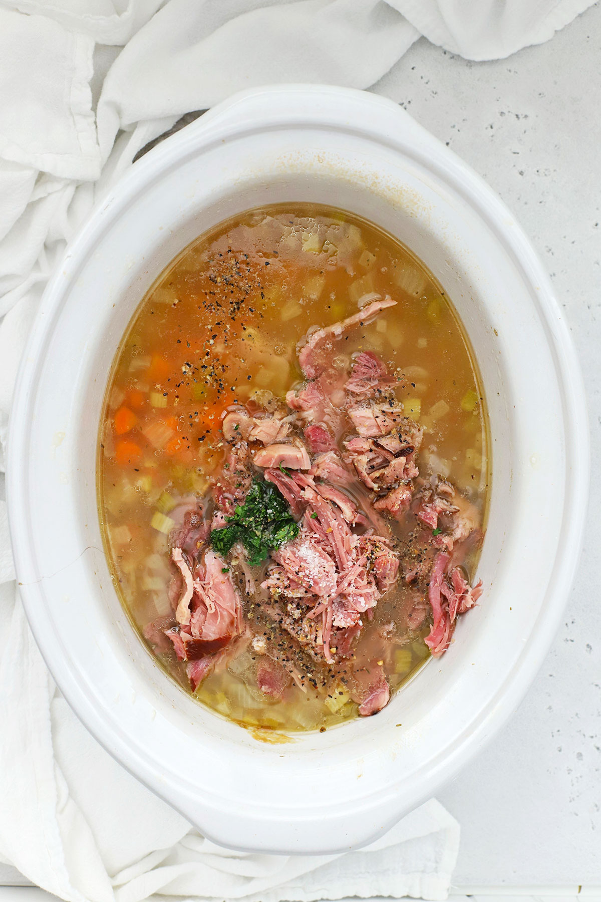 Shredding ham and adding fresh herbs and seasoning to slow cooker ham bean soup