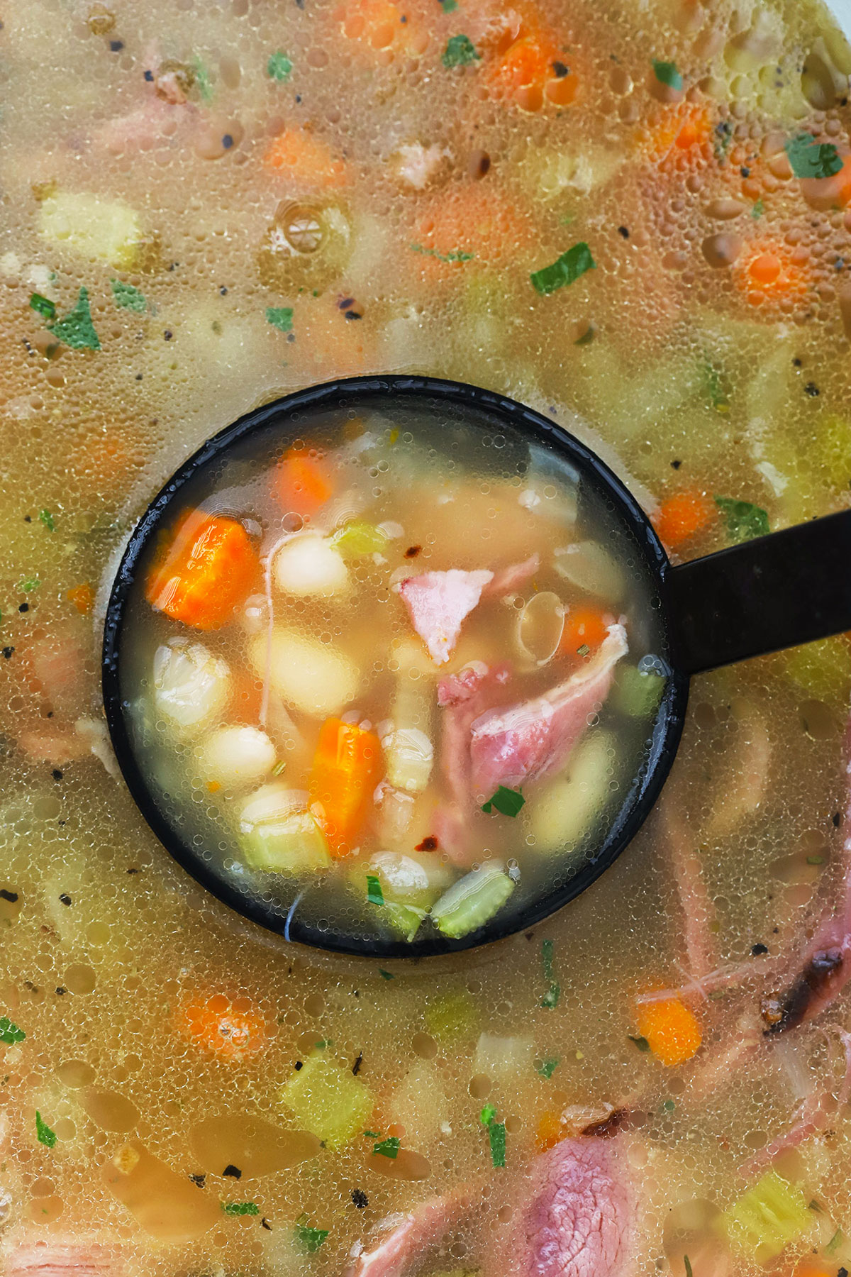 A ladle scooping up crock pot ham and bean soup